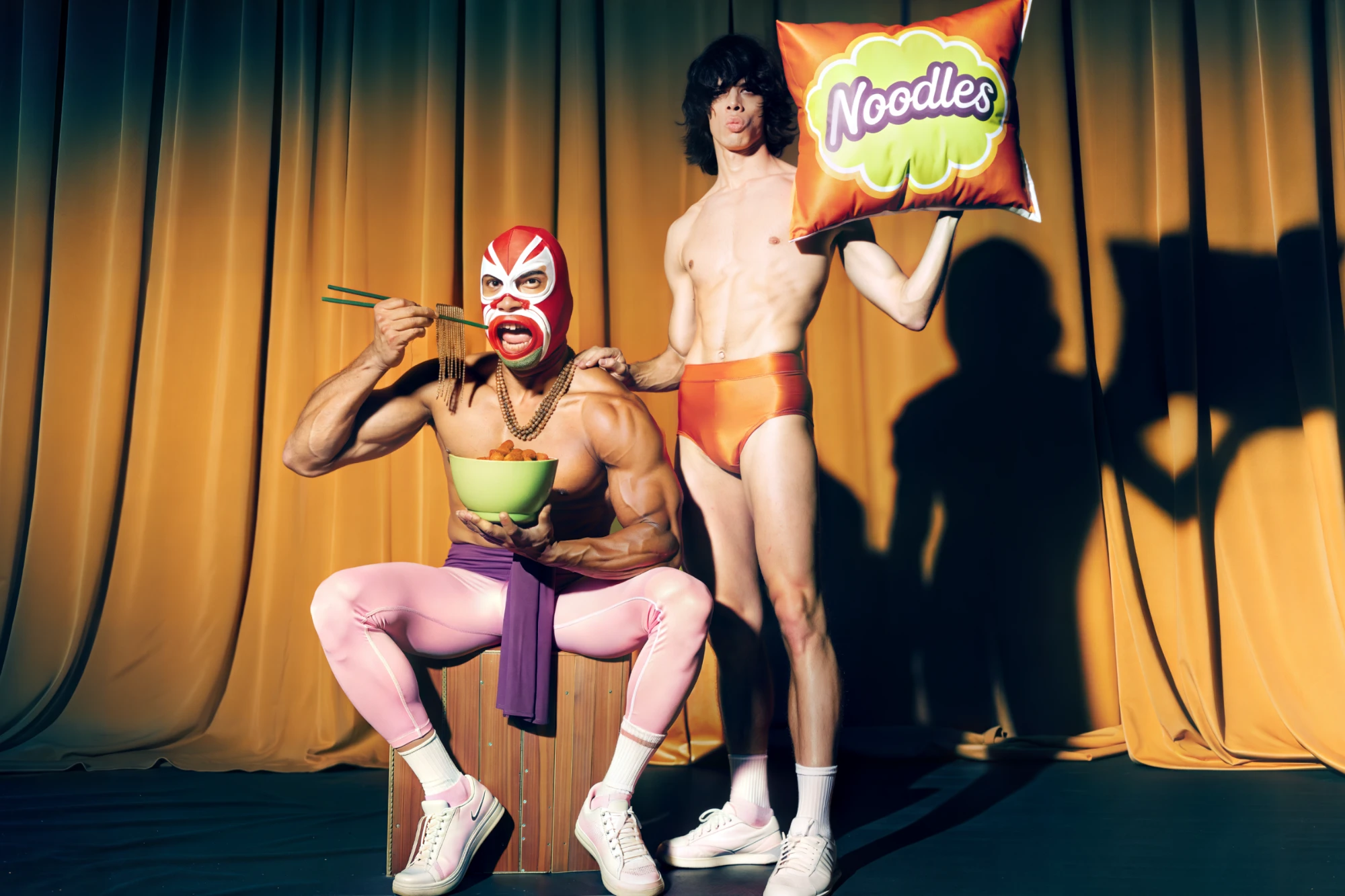 BBOKKI, a masked wrestler eating noodles on stage beside a man holding a bag